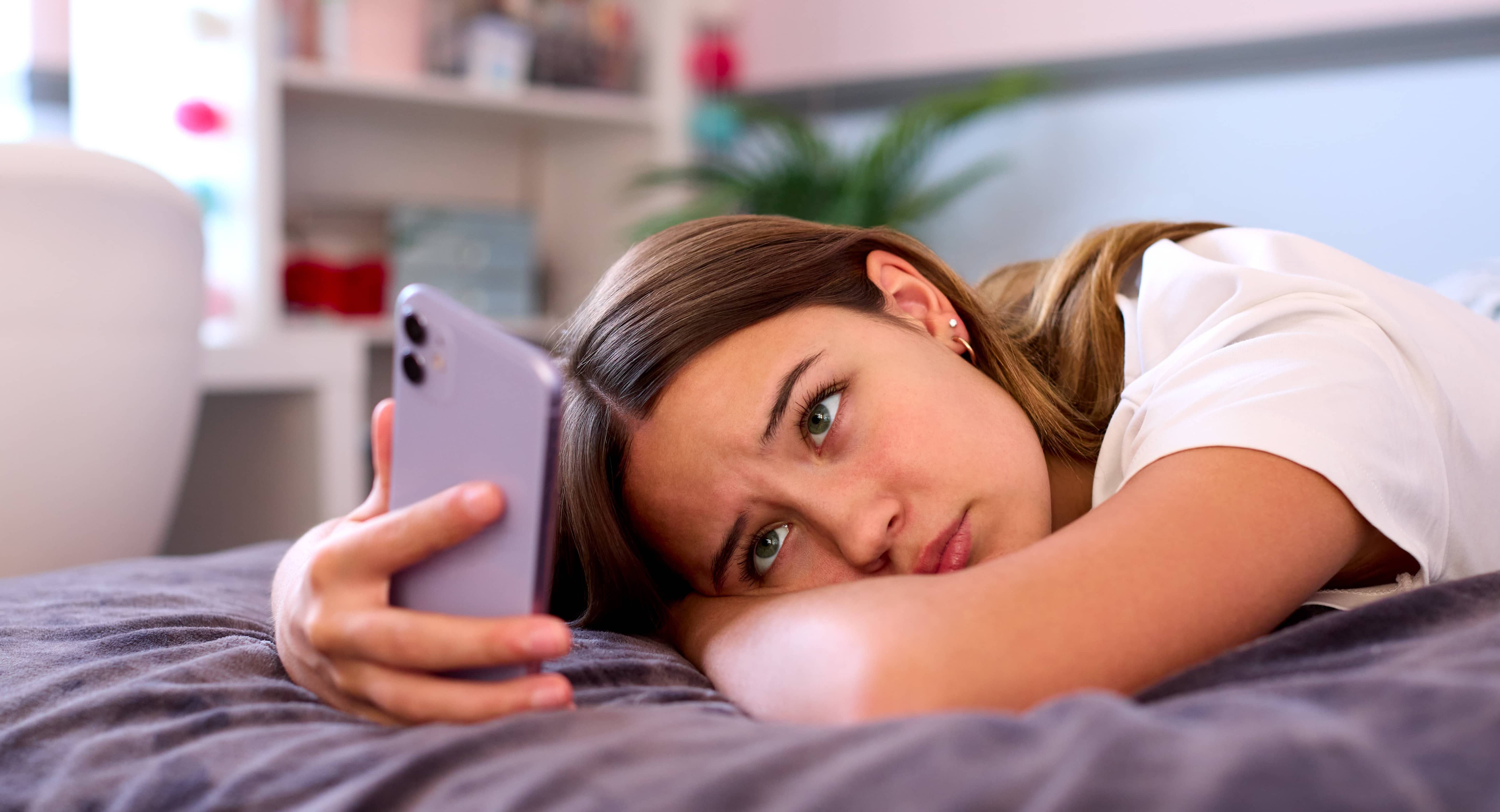 depressed-teenage-girl-lying-on-bed-at-home-looking-at-mobile-phone