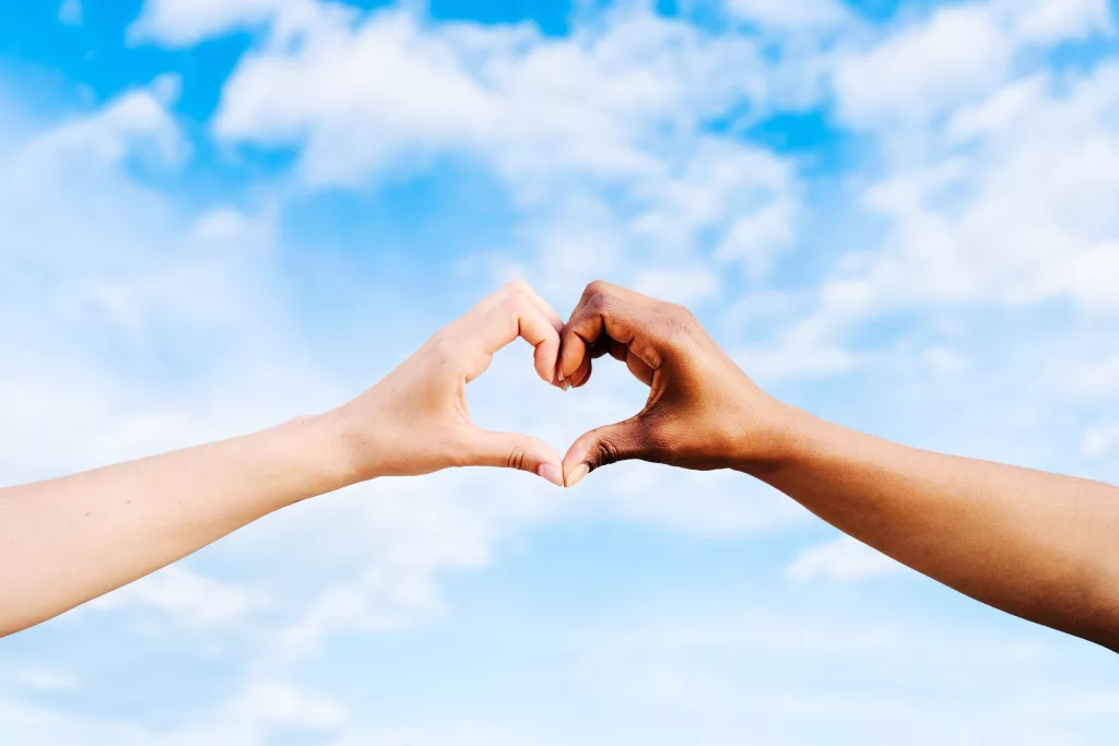 two-multiethnic-hands-join-together-to-form-a-shape-heart-with-a-blue-sky-clouds-background-concept-of-hope-and-love-between-different-races-peace-between-humans-and-against-hatred-and-racism