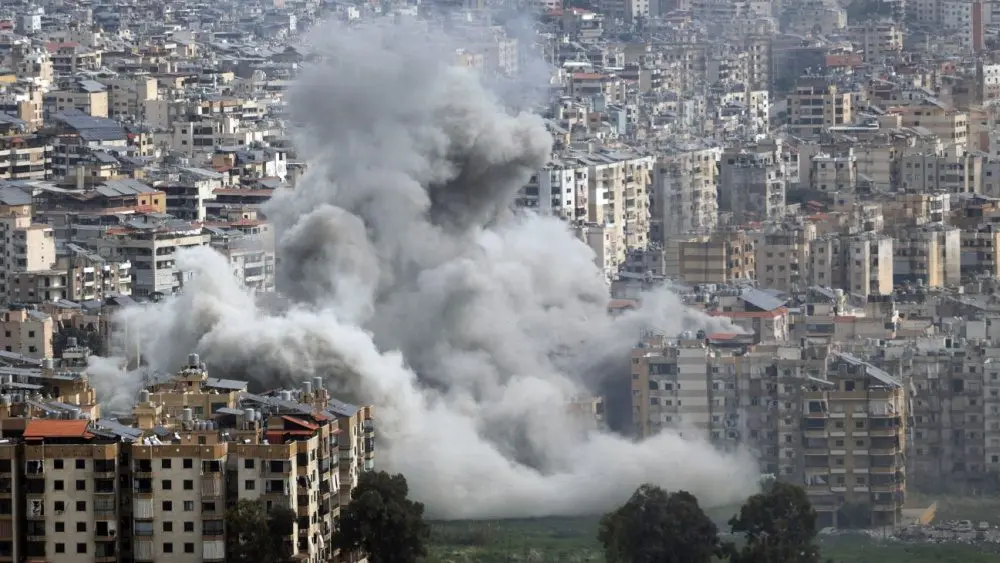Large plumes of grey smoke billow from mult story apartment buildings following an explosion in a densely populated city^ depicting the devastation of modern urban warfare. Jan 28 2026 in USA