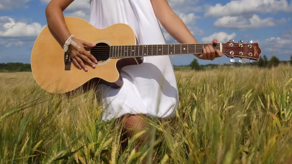 girl playing guitar in field over blue sky.