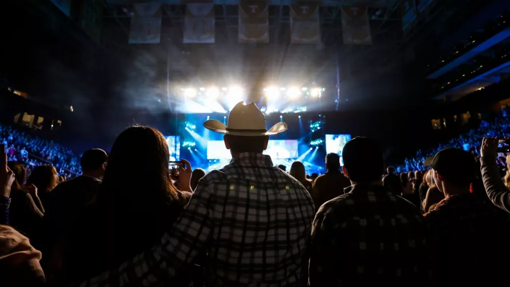 A country music fan watches a live concert wearing a cowboy hat.