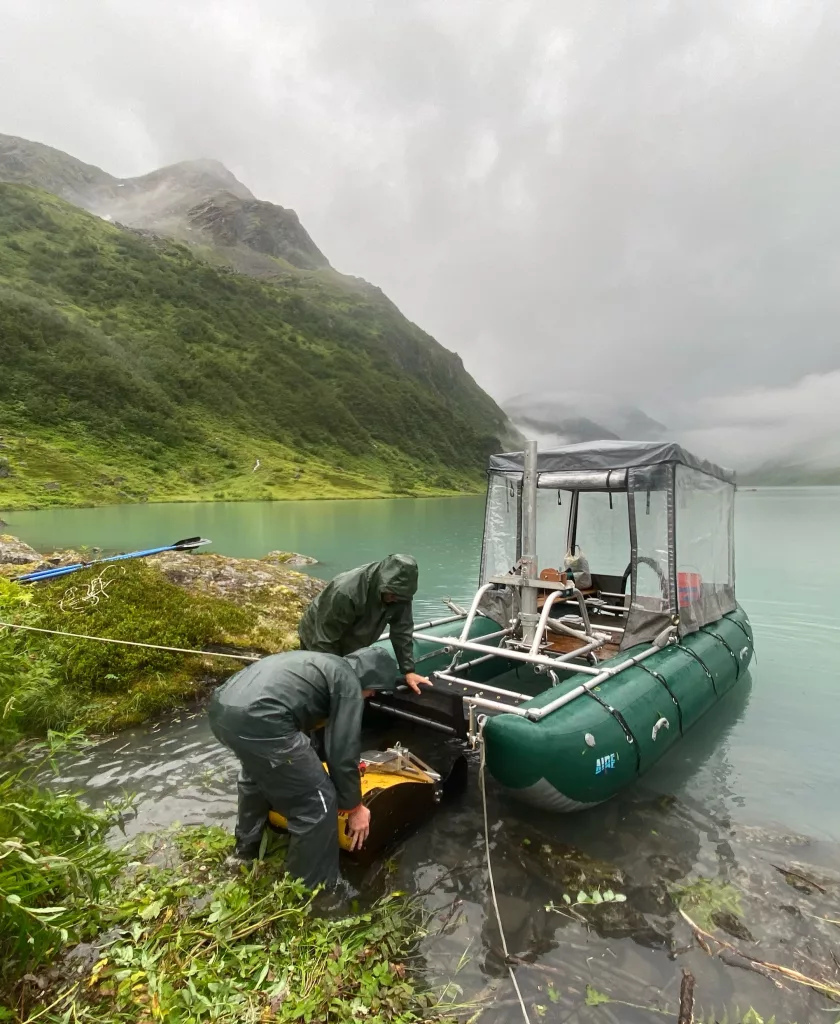 Drake Singleton, left, and Peter Haeussler install a sound wave-generating device onto a pontoon boat they carried to Allison Lake near Valdez. Photo by Gerry Hatcher.