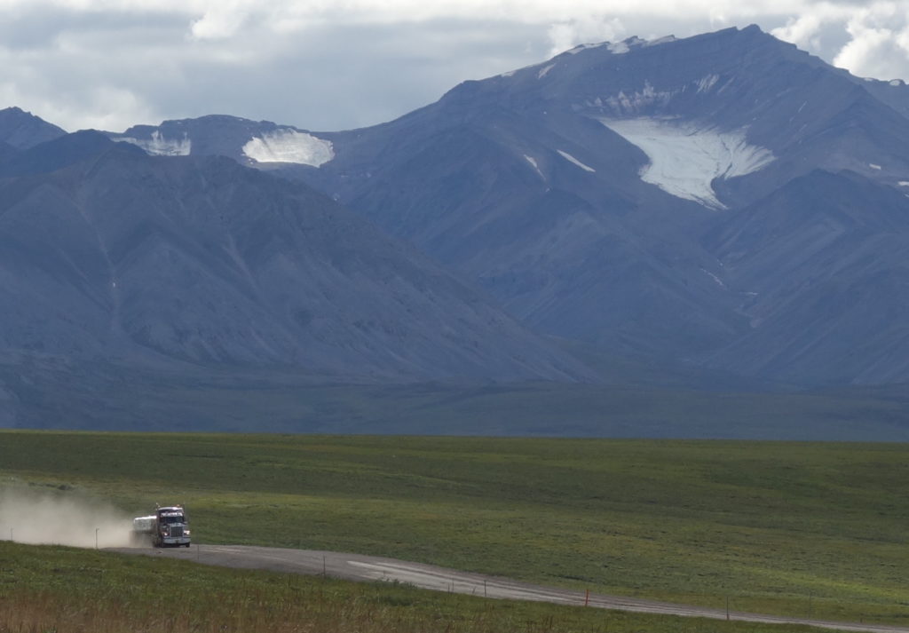 A trucker drives the Dalton Highway toward Prudhoe Bay beneath the withering Gates Glacier.