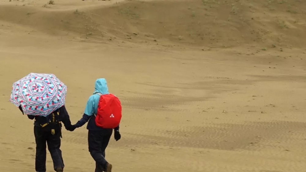 Karin Bodony, left with umbrella, hikes with her 15-year-old daughter Ida in the Nogahabara Dunes 35 miles west of Huslia. Photo by Ned Rozell.