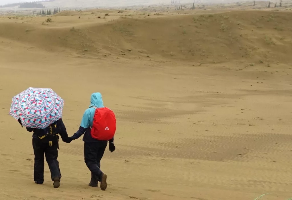 Karin Bodony, left with umbrella, hikes with her 15-year-old daughter Ida in the Nogahabara Dunes 35 miles west of Huslia. Photo by Ned Rozell.