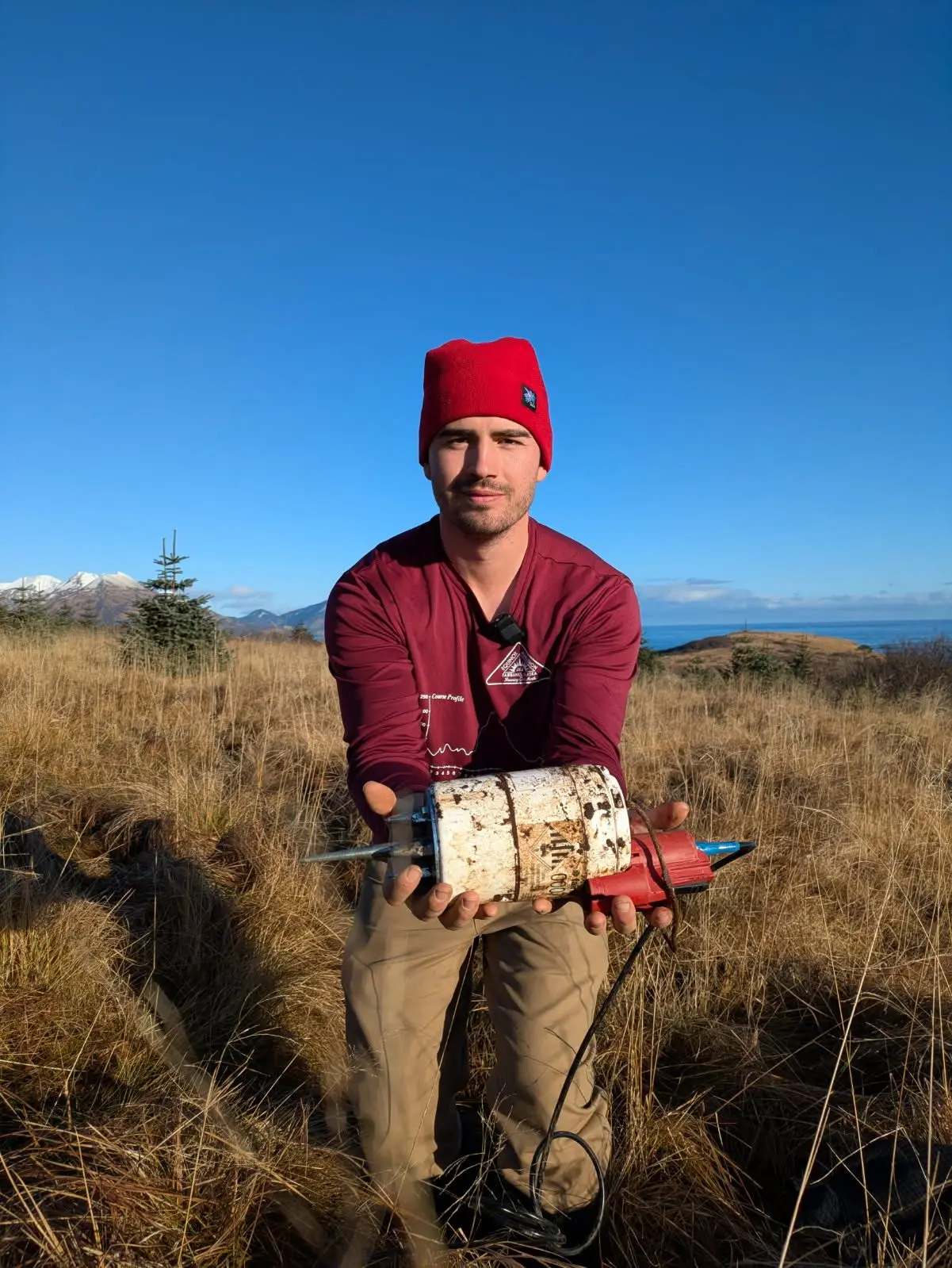 University of Alaska Fairbanks doctoral student Cade Quigley holds a freshly unearthed seismic sensor in Kodiak in November 2025. Photo by Sara Wilbur