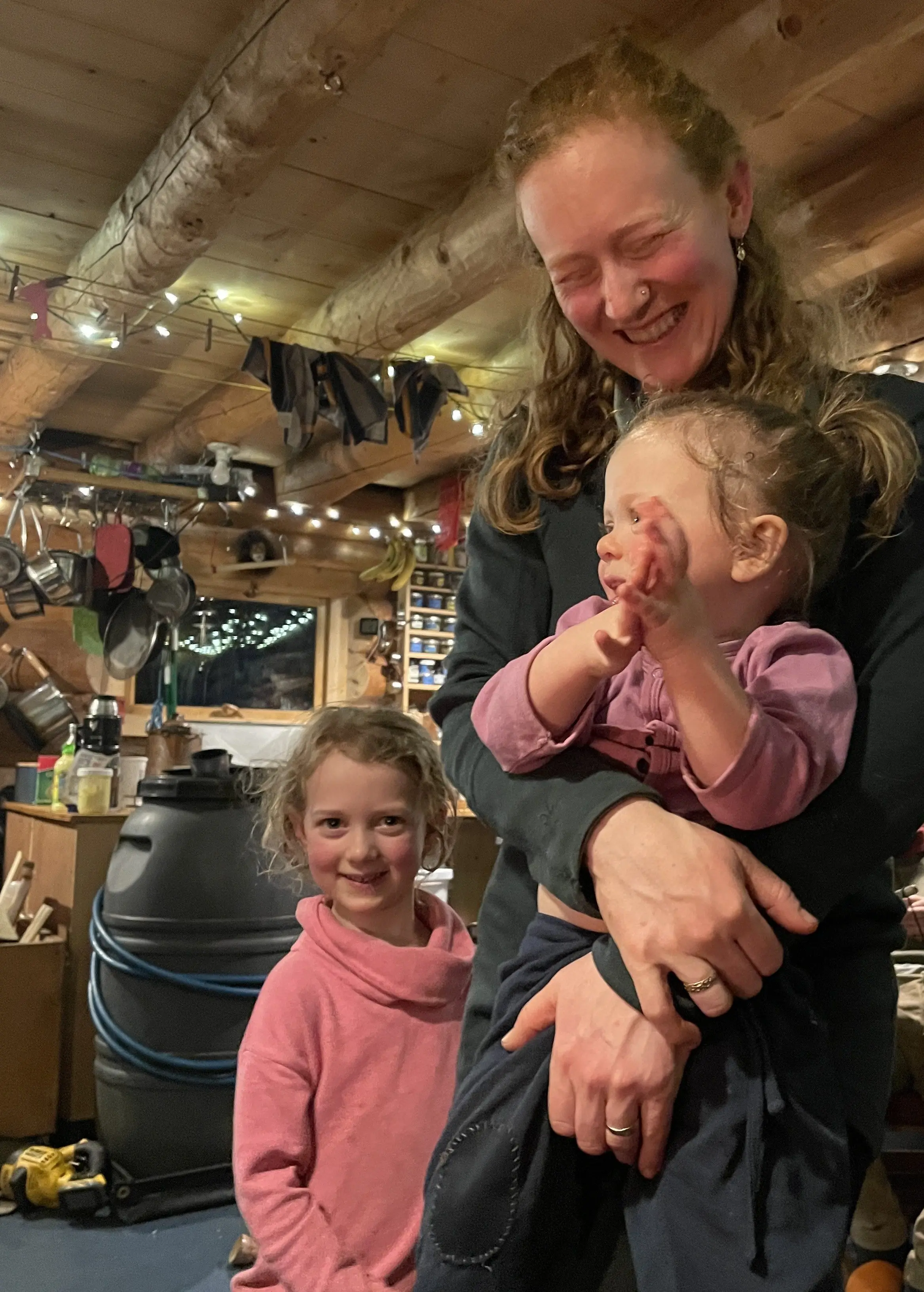 Jenna Jonas holds her daughter Juniper while her other daughter Celia looks on. Jenna and David Jonas hosted Ned and Forest at their Tanana River homestead on the first night of the bikers’ trip. Photo by Ned Rozell.
