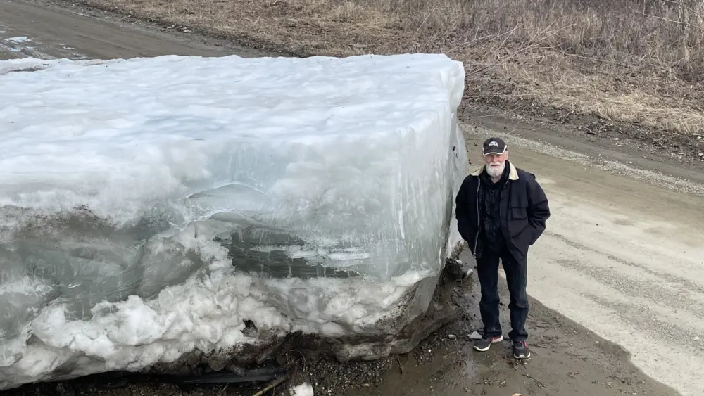 Eagle resident Steve Hamilton stands next to a block of Yukon River ice that the river lifted onto a road there on May 12, 2023. Photo by Ned Rozell.