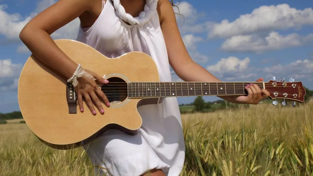 woman in field playing guitar in white dress