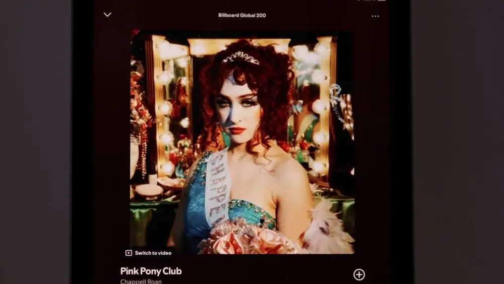An Apple iPad displays the Spotify music streaming app. The screen the shows the song "Pink Pony Club" by "Chappell Roan" being played^ as well as the album cover art.