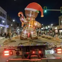 Giant illuminated gingerbread man inflatable on a flatbed trailer rolls through downtown Galesburg during the nighttime Holly Days Parade^ with crowds lining both sides of the snow-dusted street and holiday lights glowing in the background. (Photo: Steve Davis/seedcophoto.com)