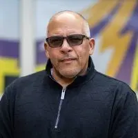 Portrait of Adam Gonzaga^ the new head football coach at Knox College^ standing in front of the Prairie Fire logo.