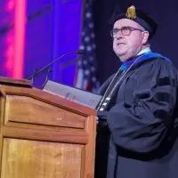 ALT TEXT: Seamus Reilly in academic regalia speaking at a podium during a Carl Sandburg College graduation ceremony
