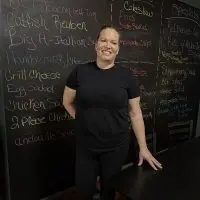 Christie Harris standing in front of a chalkboard menu at The Flavor District