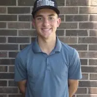 Aidan Nelson wearing a golf polo and cap in front of a brick wall