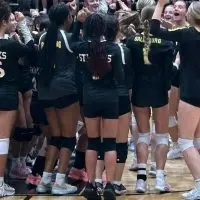 ALT TEXT: Galesburg High School volleyball players in black Streaks jerseys celebrating in a group on the gym floor