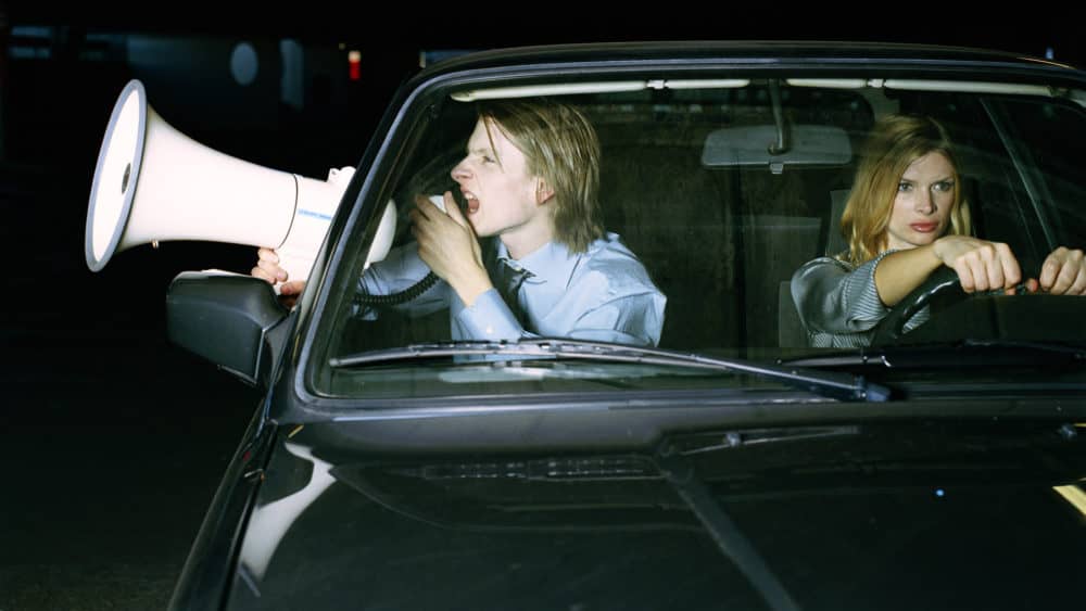 man-and-woman-in-car-man-using-megaphone-through-open-window