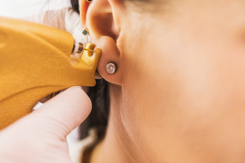 a-doctor-in-sterile-white-medical-gloves-pierces-the-ears-of-a-young-girl-in-the-medical-office-with-a-piercing-gun