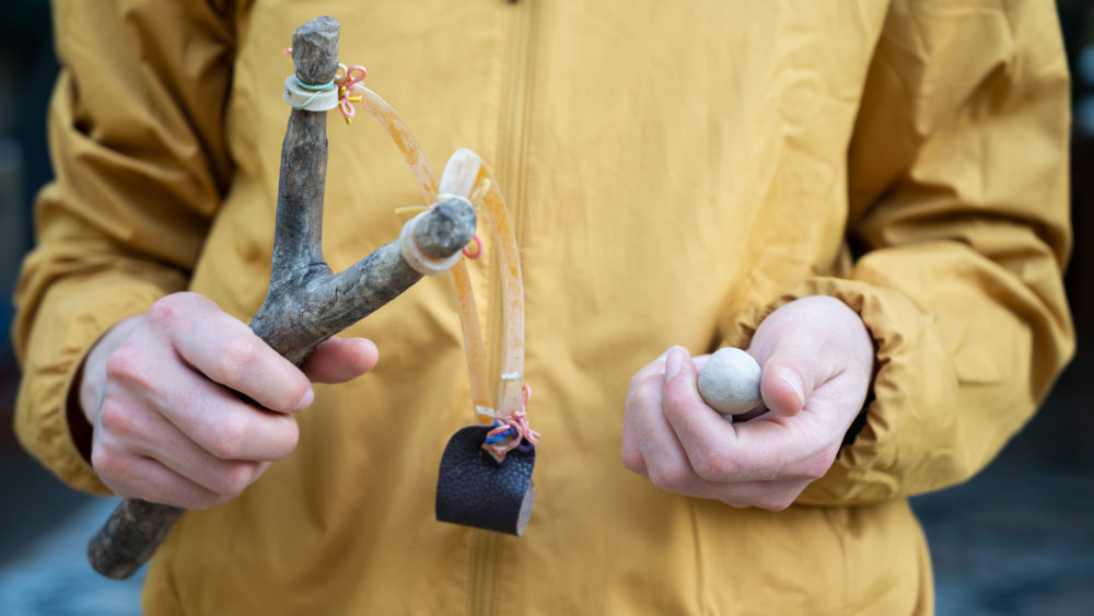cropped-shot-of-woman-holding-a-wood-slingshot-with-clay-bullet-in-her-hands-a-slingshot-works-like-a-small-catapult-with-rubber-strips-holding-a-stone-or-other-projectile-sits