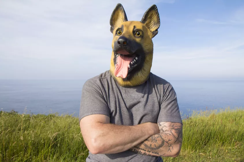 man-with-tattooed-arm-and-german-shepherd-dog-mask-with-arms-crossed-by-the-sea