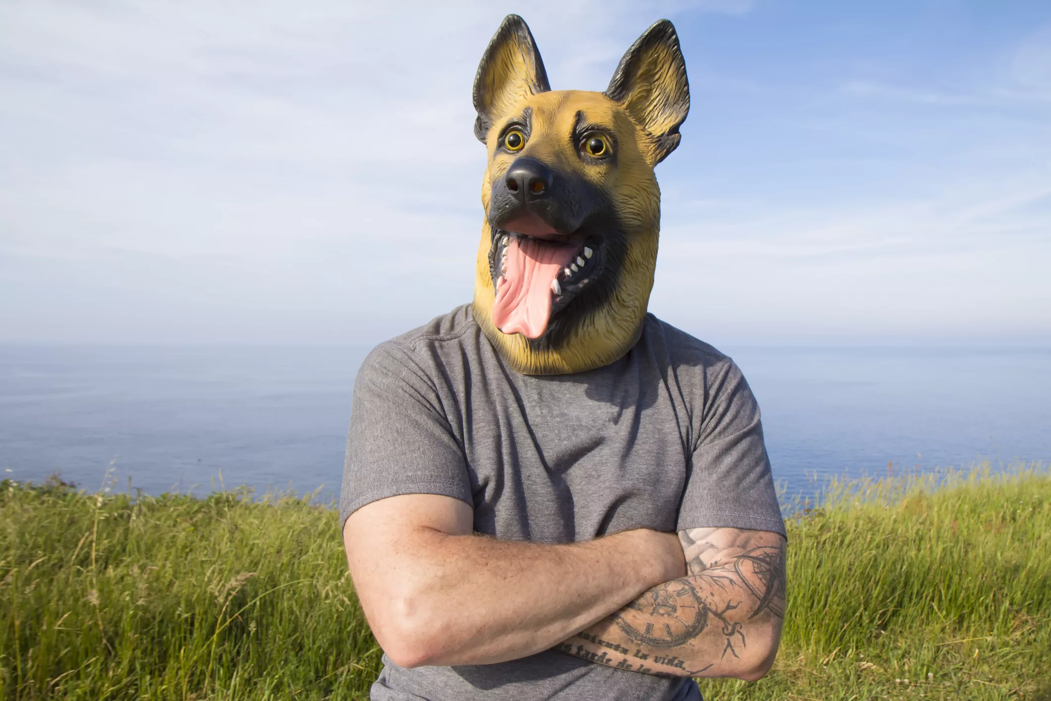 man-with-tattooed-arm-and-german-shepherd-dog-mask-with-arms-crossed-by-the-sea