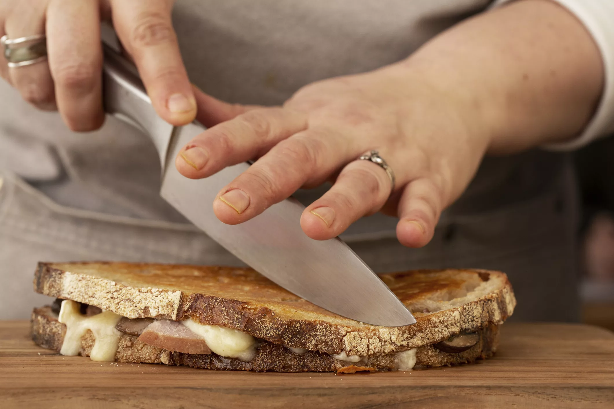 close-up-of-person-slicing-toasted-sourdough-cheese-melt-with-chefs-knife