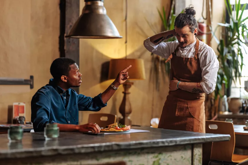 angry-african-american-man-complaining-over-dish-to-ashamed-hispanic-waiter