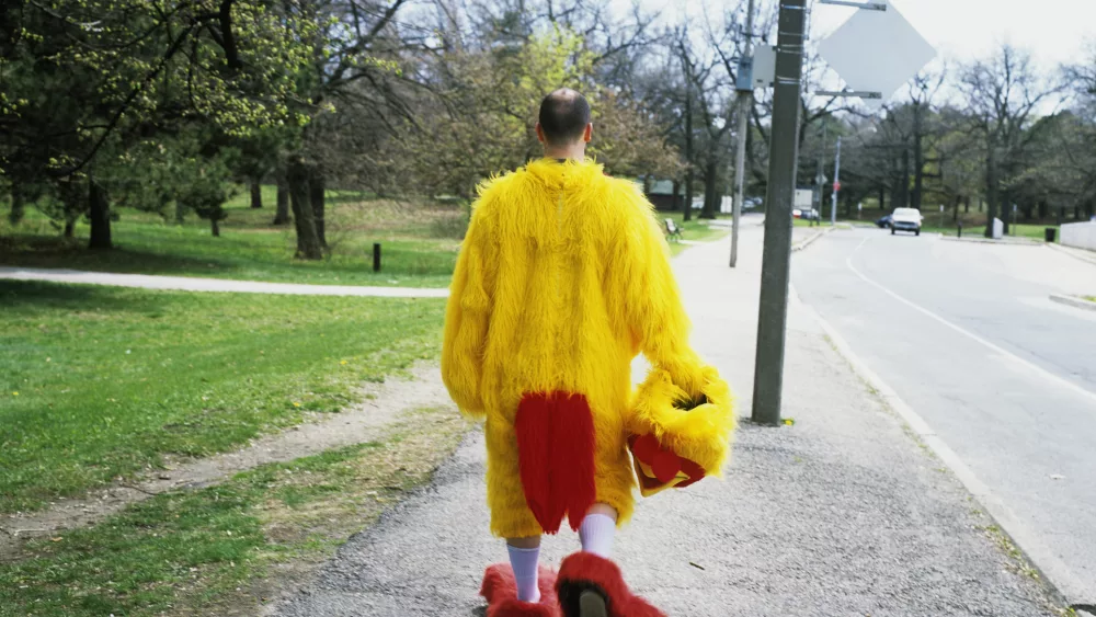 man-in-chicken-suit-walking-in-park-rear-view