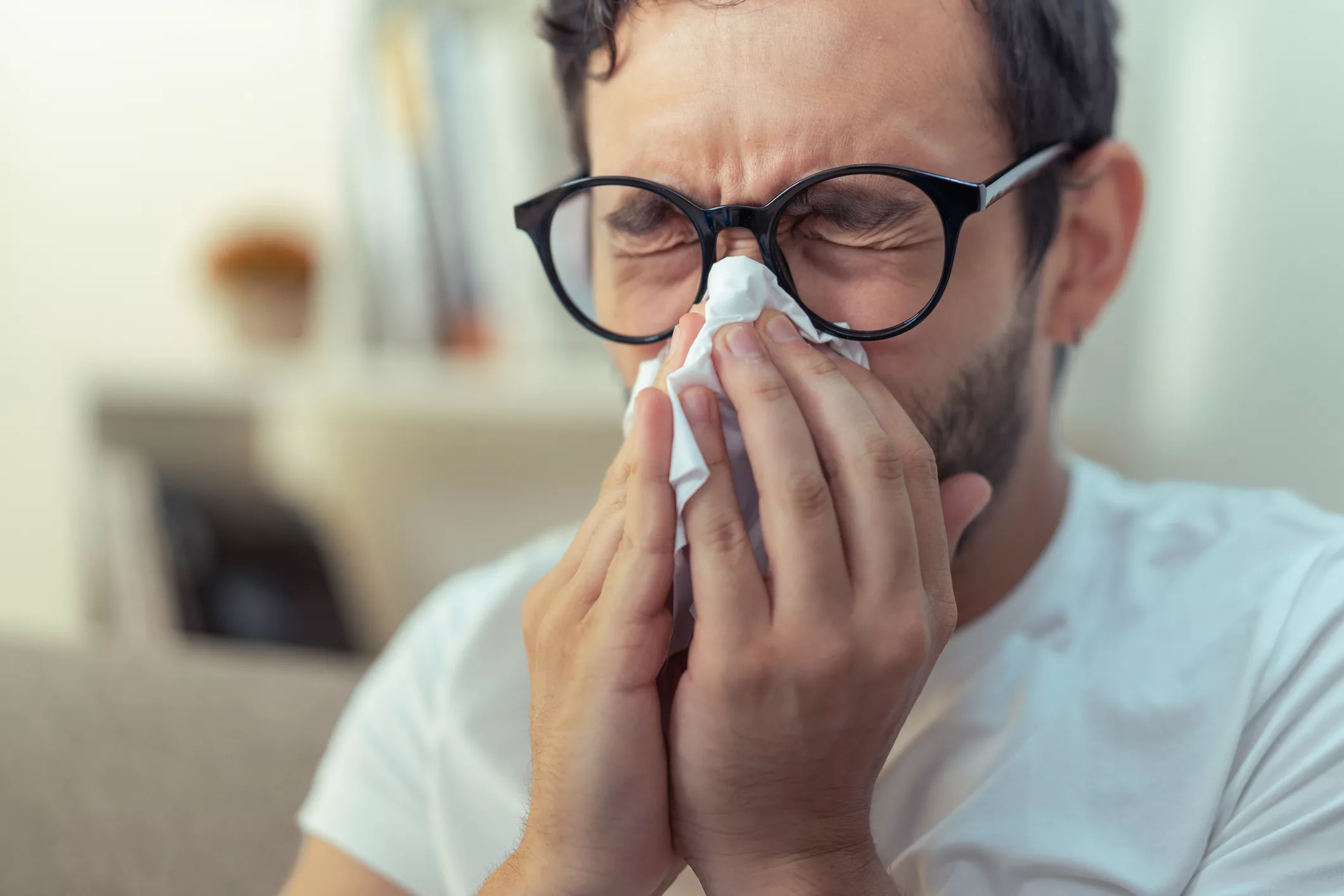 young-man-sneezing-wiping-his-nose-with-a-piece-of-tissue-paper