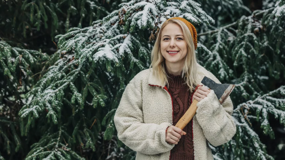 smiling-woman-with-blond-hair-holding-axe-in-front-of-christmas-tree