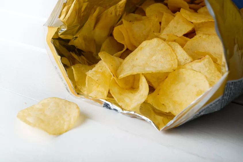 crispy-fried-greasy-potato-chips-fall-out-or-are-spilled-out-of-the-package-on-a-white-background-or-table-the-concept-of-unhealthy-diet-and-lifestyle-accumulation-of-excess-weight