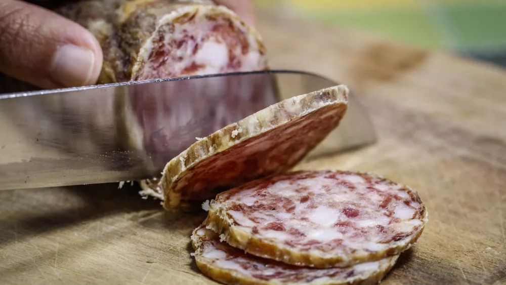 artisanal-friulian-salami-being-sliced-on-a-rustic-wooden-cutting-board