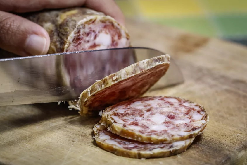 artisanal-friulian-salami-being-sliced-on-a-rustic-wooden-cutting-board