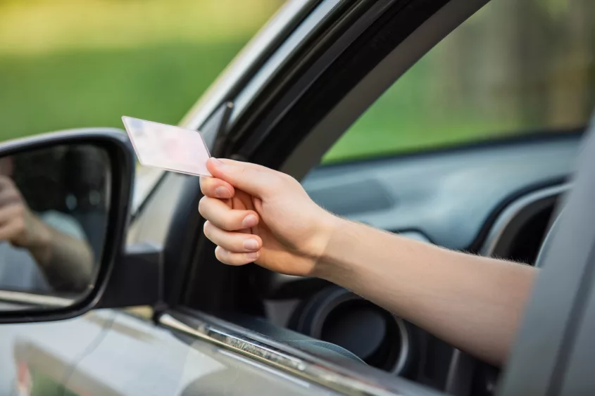 close-up-person-hand-out-of-the-car-window-holding-the-driver-license-as-shows-it-to-the-police-officer-for-control