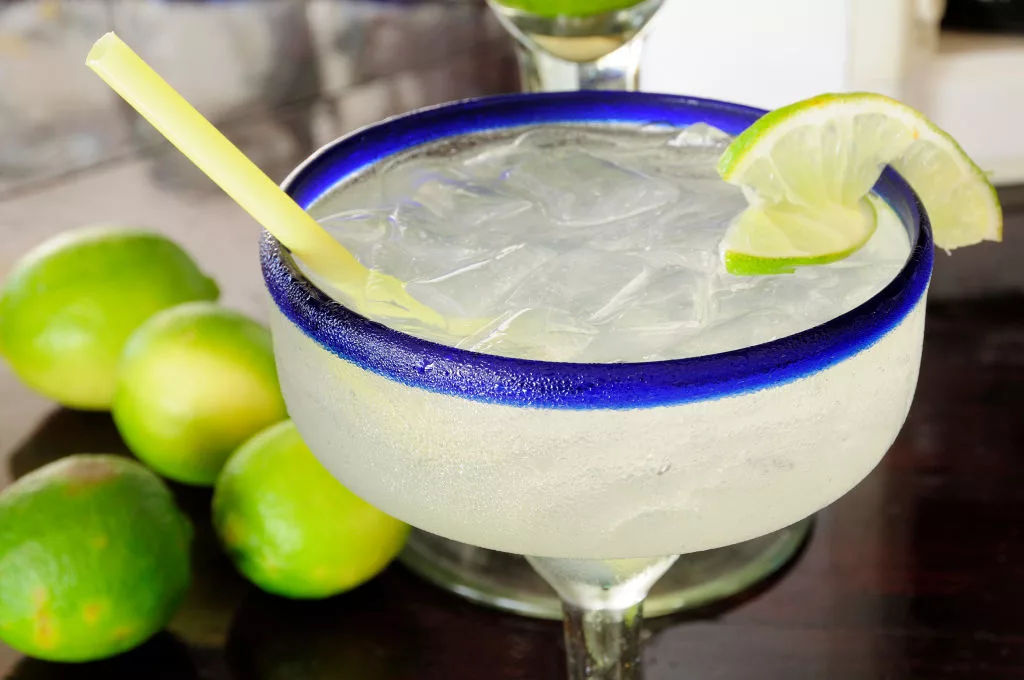 frosted-glass-of-a-margarita-cocktail-served-with-ice-and-slice-of-lime-with-whole-limes-at-side