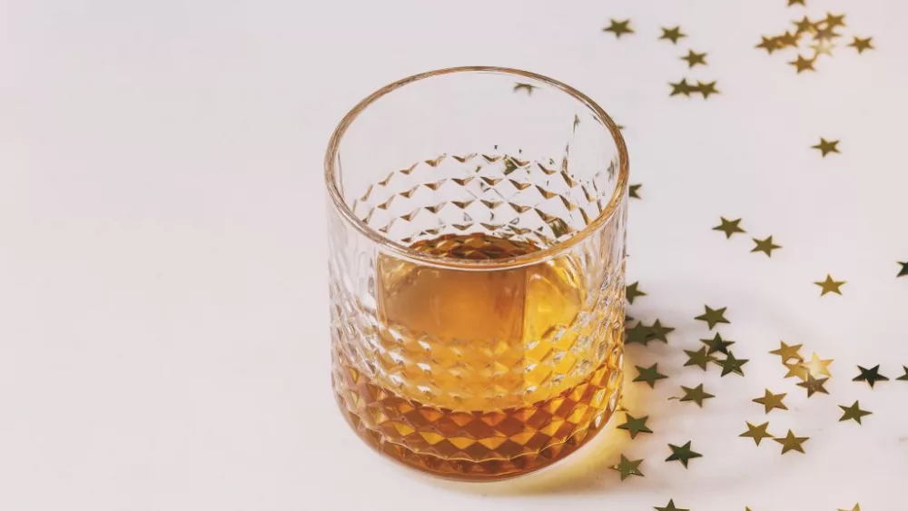 glass-of-scotch-whiskey-standing-on-white-marble-background-with-golden-holiday-christmas-stars-confetti-holidays-alcohol-drink