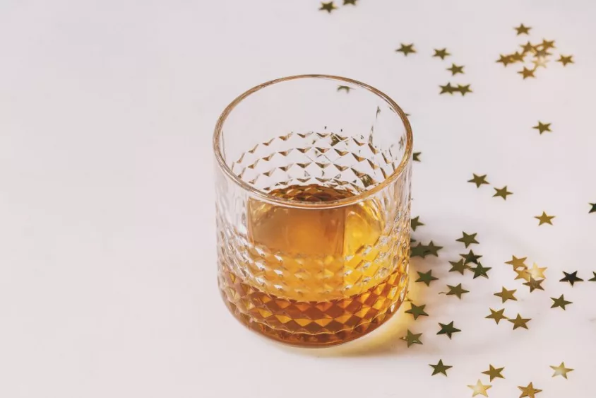 glass-of-scotch-whiskey-standing-on-white-marble-background-with-golden-holiday-christmas-stars-confetti-holidays-alcohol-drink