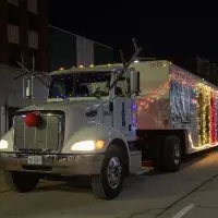 Lit-up semi-truck float from G & M Distributors with reindeer antlers^ red nose^ and colorful lights on the trailer during the 2025 Galesburg Holly Days Parade^ with crowds lining the street. (Photo: Steve Davis/seedcophoto.com)