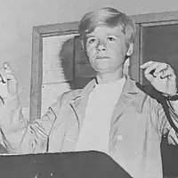 Alt text: Sally Rynott conducts the Galesburg High School band^ baton in hand at the podium