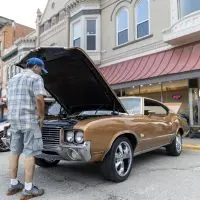 Man looking under the open hood of a gold Oldsmobile Cutlass