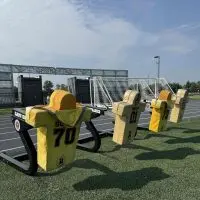 ALT TEXT: Football blocking sleds with padded dummies on the turf at CBI Bank & Trust Stadium