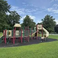 Playground equipment with slides and climbing features at Lincoln Park^ with the pool visible in the background
