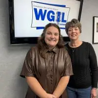 Two women smile in front of a screen showing the WGIL logo in the station’s studio.