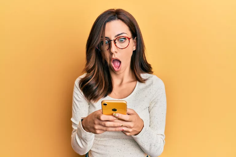 young-brunette-woman-using-smartphone-over-yellow-background-afraid-and-shocked-with-surprise-and-amazed-expression-fear-and-excited-face