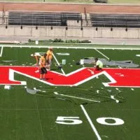 Workers install the new varsity 'M' logo on the Bobby Woll Memorial Field turf on June 12.