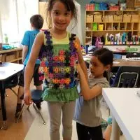 Young girl wearing colorful Lux Blox creation in classroom