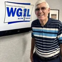 Jim Reinebach smiling in front of the WGIL logo at the station's Galesburg studios.