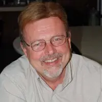 Doug Ferreter smiling^ wearing glasses and a checkered button-down shirt