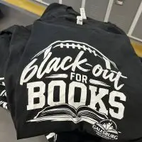 Folded black T-shirts printed with a football^ an open book and the words "Black-out for Books" above the Galesburg Public Schools Foundation logo