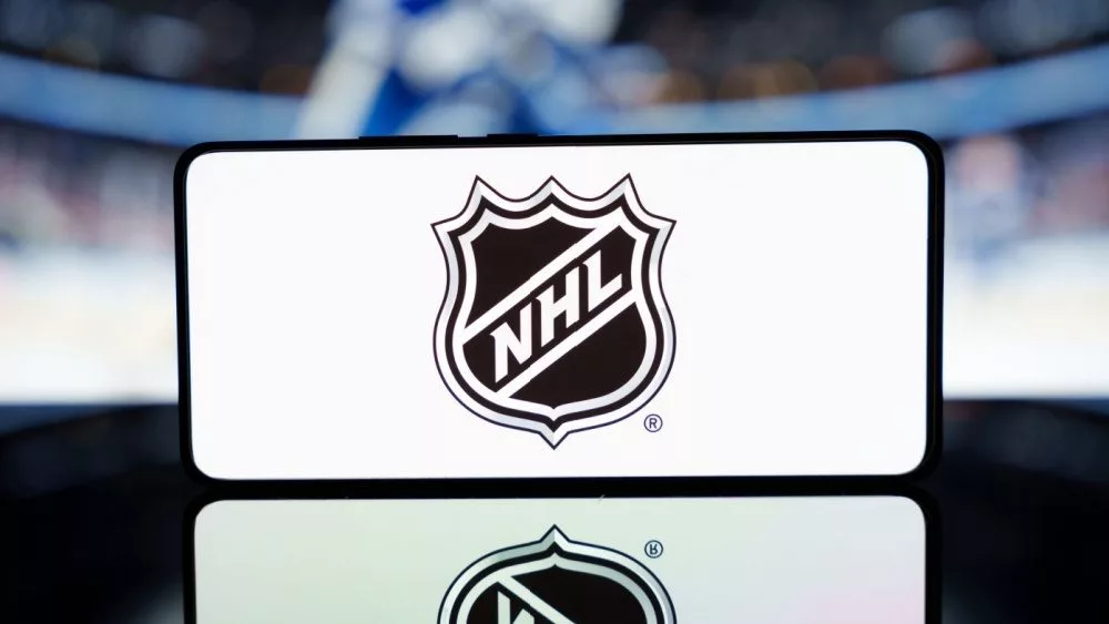 A smartphone displaying the NHL logo with a blurred hockey game in the background. January 13^ 2025